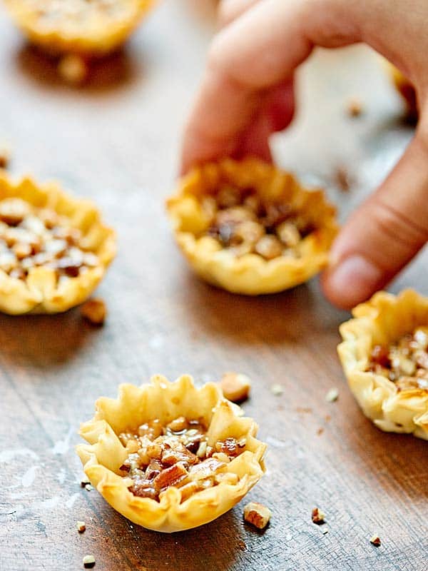 pecan pie bites on counter, one being picked up