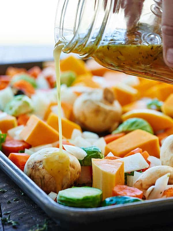 dressing being drizzled over veggies on baking sheet