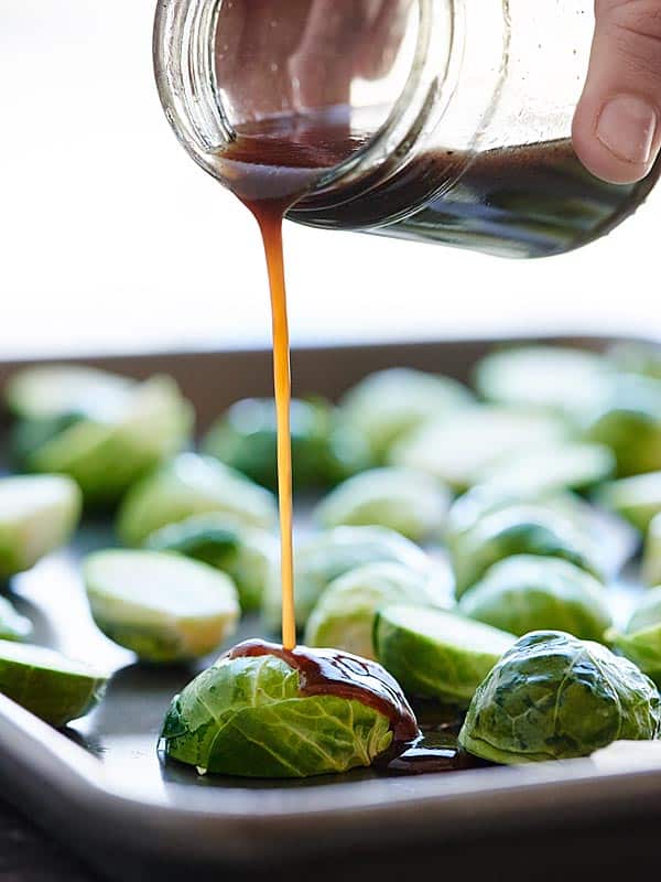 balsamic vinegar being drizzled over baking sheet of brussels sprouts