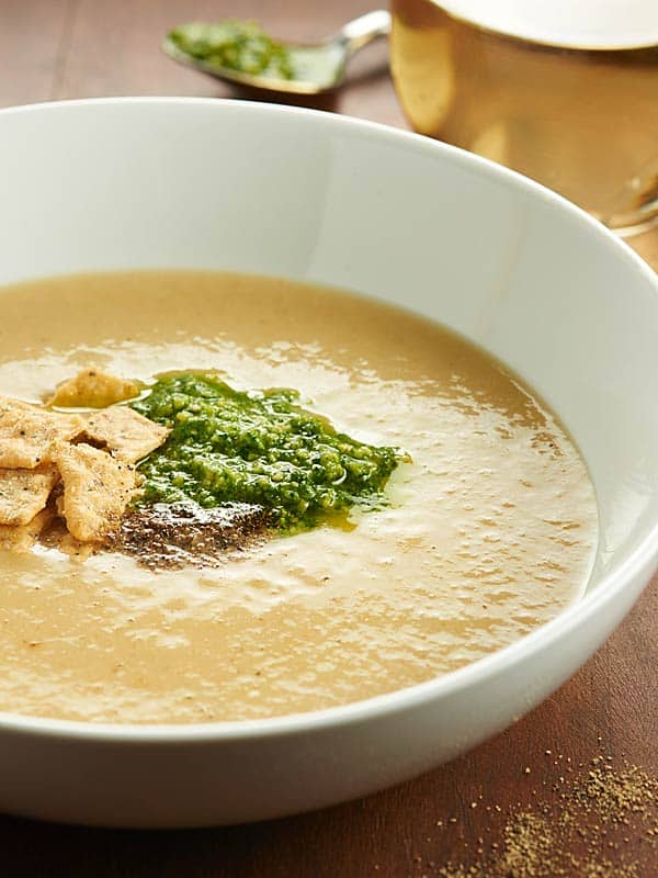 bowl of cauliflower leek soup garnished with crackers and cilantro pesto