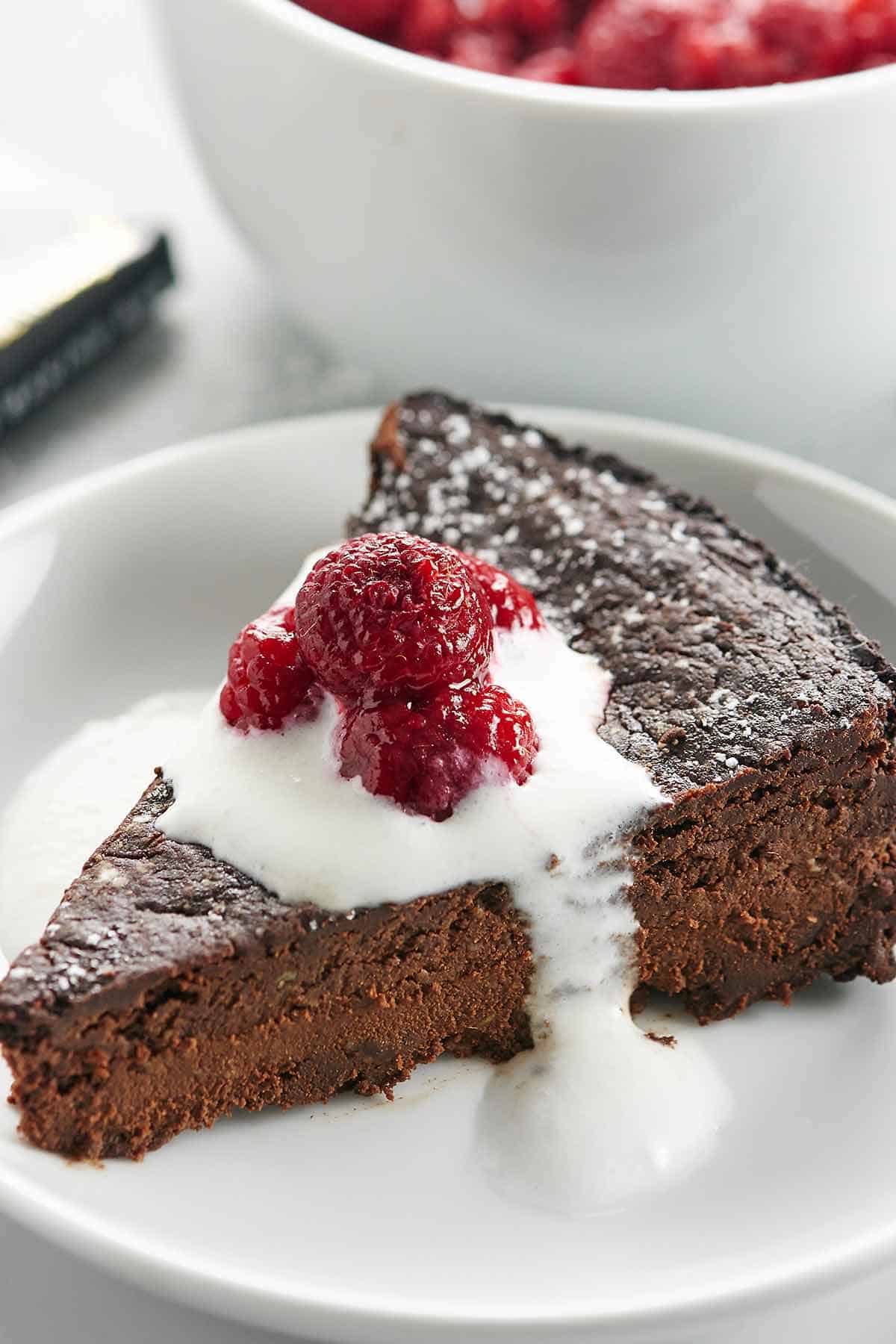 Slice of vegan chocolate cake with icing and raspberries on plate