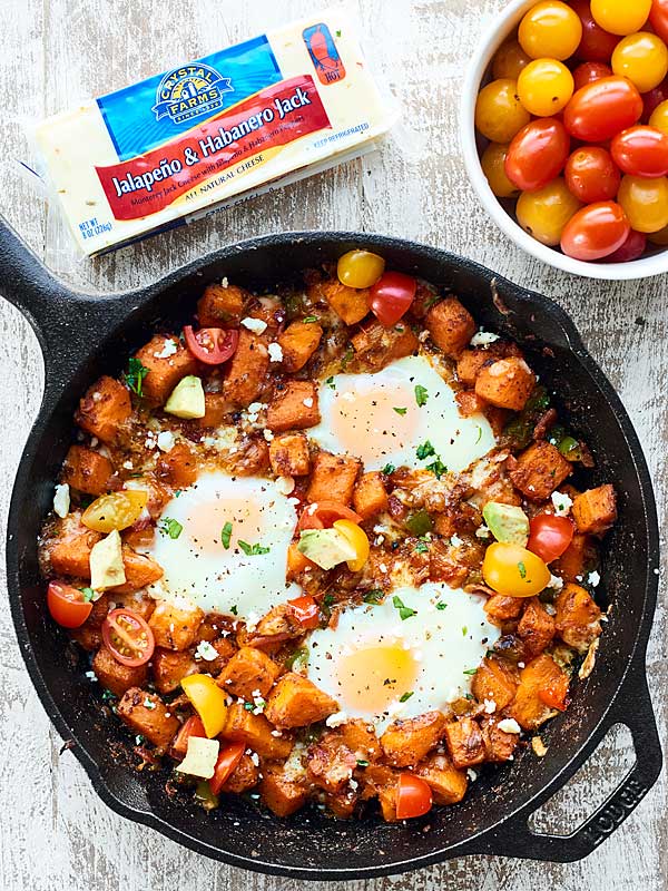 Skillet of sweet potato hash next to Crystal Farms cheese and a bowl of cherry tomatoes