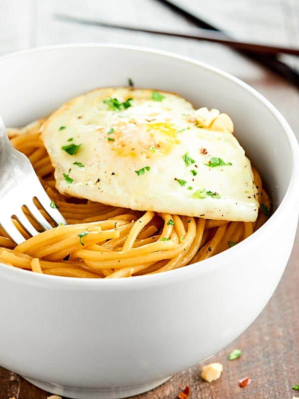 Bowl of thai peanut noodles with fork and fried egg