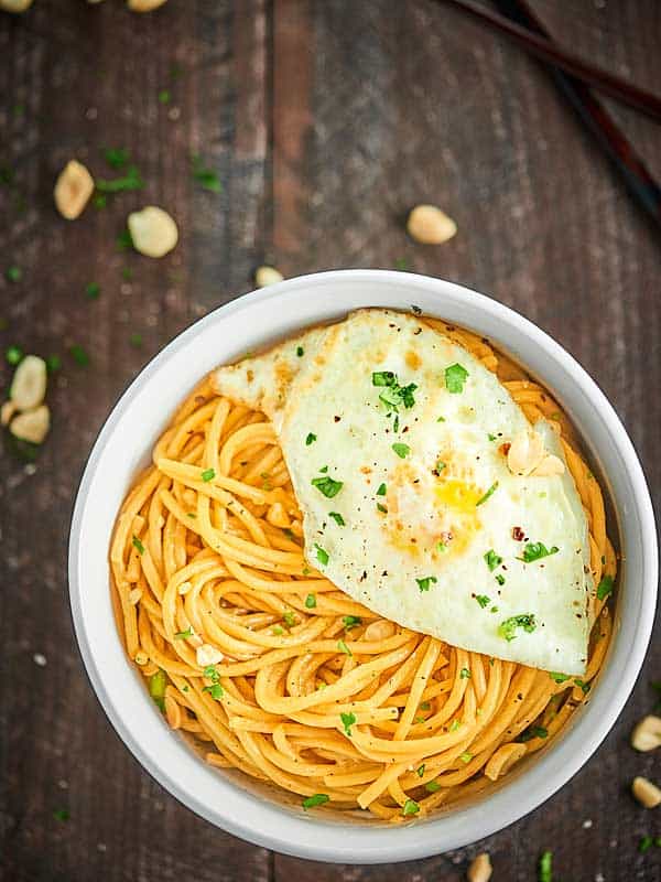 Bowl of thai peanut noodles with egg above 