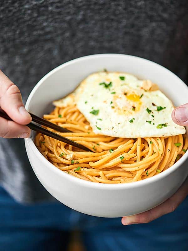 Bowl of thai peanut noodles with chopsticks and egg on top held