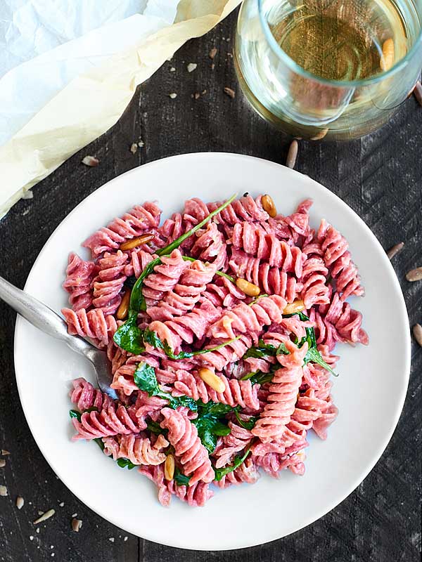  plato de pasta de remolacha junto a una copa de vino blanco arriba