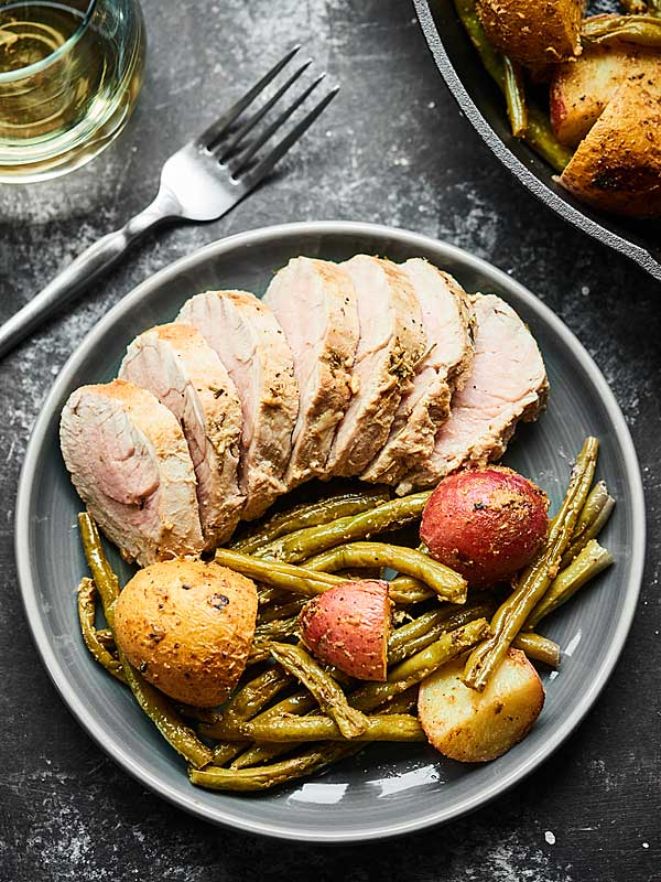 Baked pork tenderloin on plate with roasted potatoes and green beans above