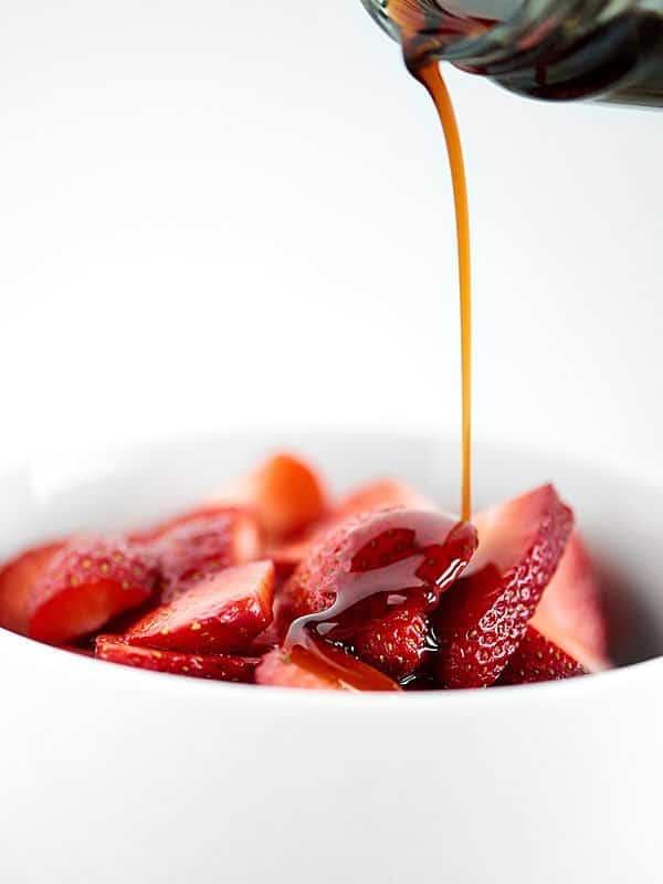 balsamic vinegar being poured over sliced strawberries