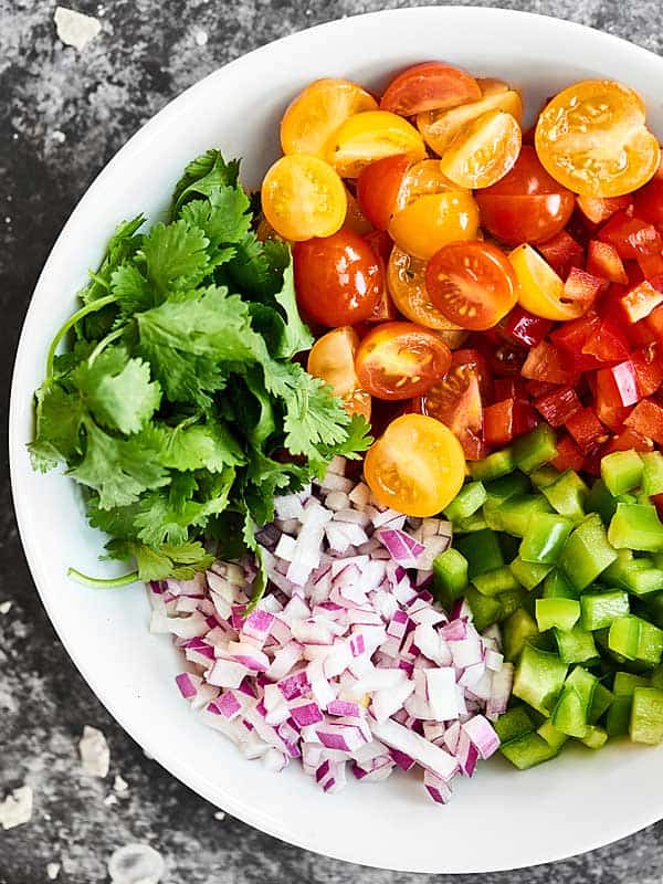 Tomatoes, peppers, onion, and cilantro separated on a plate from above 