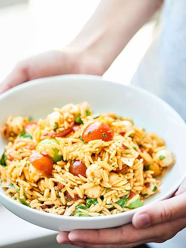 bowl of caprese pasta salad held two hands