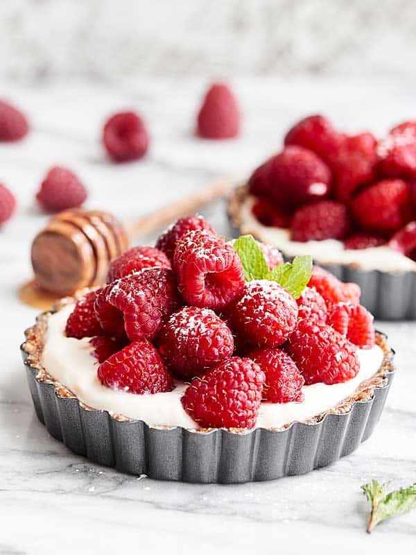 Fruit tart topped with raspberries, another in background