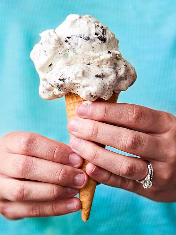 no churn mint oreo ice cream in cone held two hands, teal background