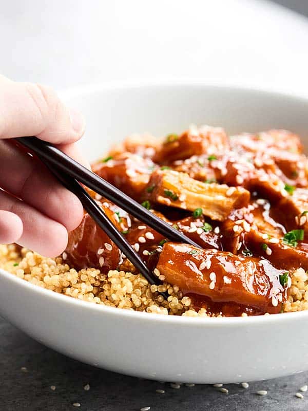 Piece of chicken being picked up out of bowl with chopsticks 