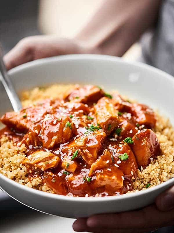 Honey sriracha chicken over quinoa in a bowl held