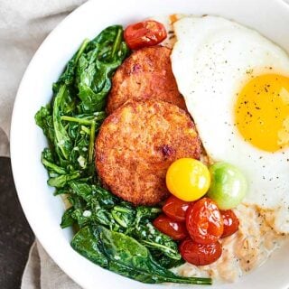 Creamy parmesan oats are topped with garlicky greens, crispy hash browns, fresh tomatoes, and a runny egg to make this the BEST Vegetarian Breakfast Bowl Recipe. showmetheyummy.com #ad #breakfastbowl @drpraegers