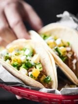 two pork carnitas tacos in a basket topped with pineapple salsa