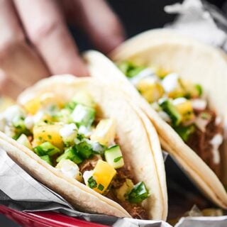 two pork carnitas tacos in a basket topped with pineapple salsa