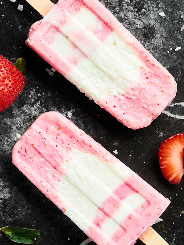 two strawberry coconut popsicles on counter above