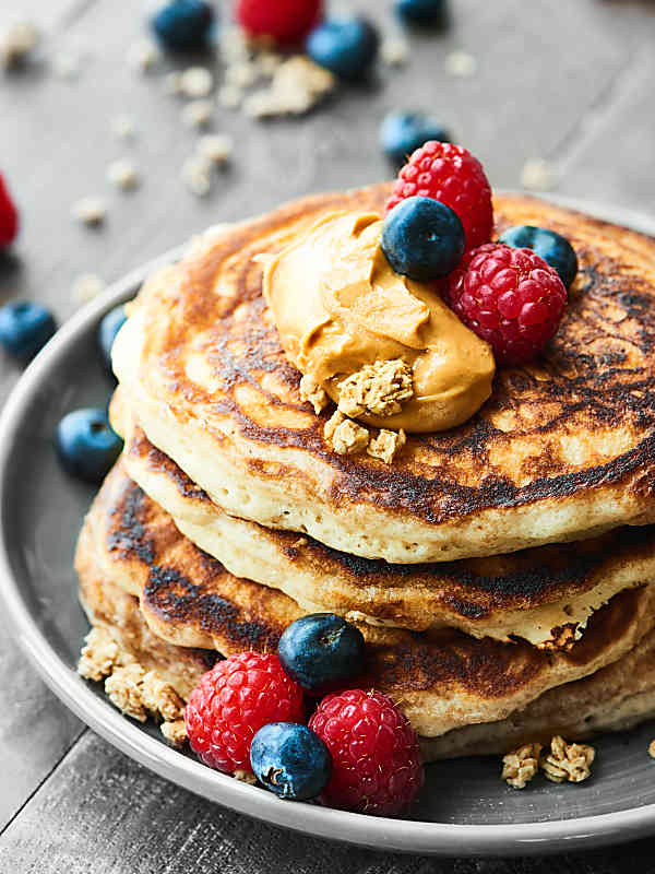 stack of pancakes on plate with berries and peanut butter