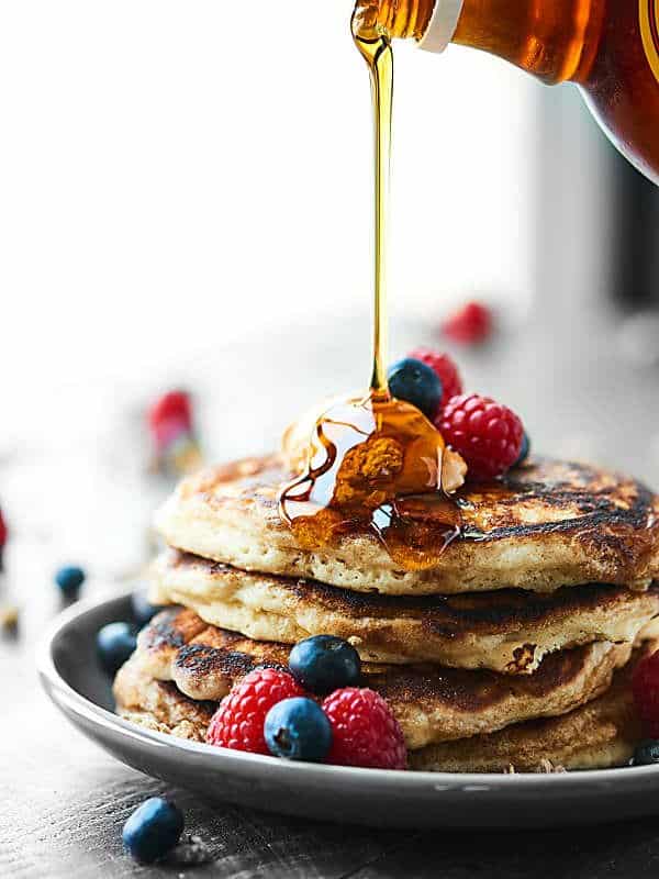 maple syrup being drizzled on stack of pancakes on plate