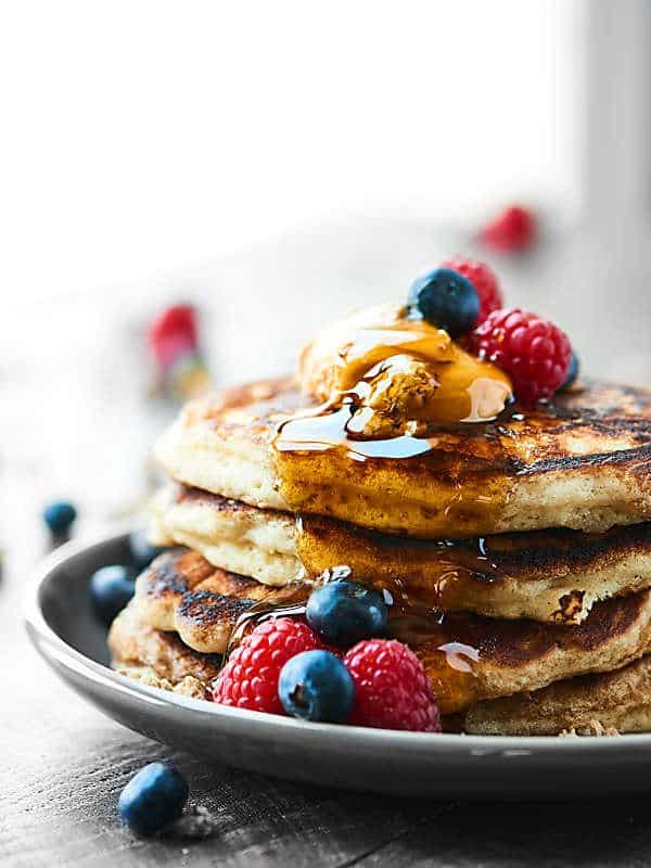 stack of pancakes on plate with syrup, peanut butter, and berries side view