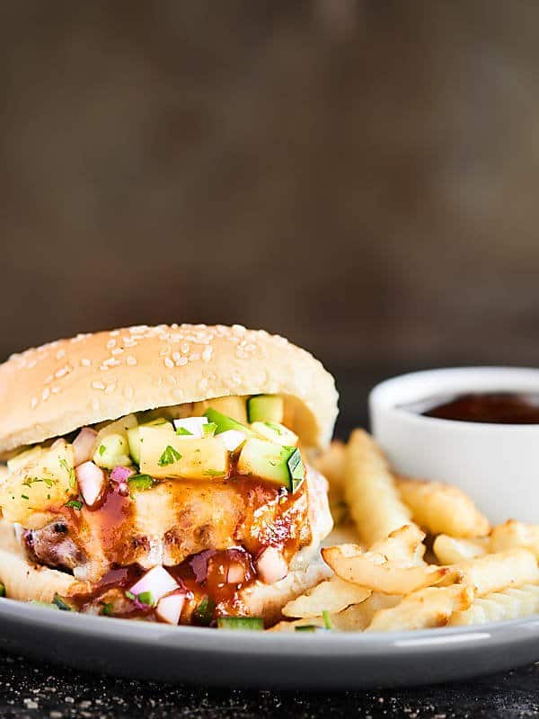 Pork burger side view on a plate with fries and bbq sauce