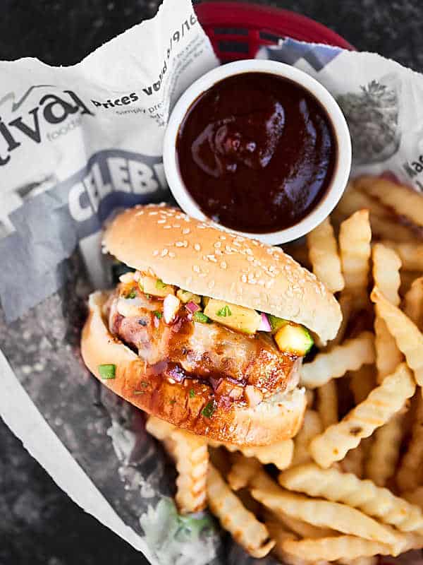 Pork burger in a basket with newspaper, side of fries and bbq sauce above