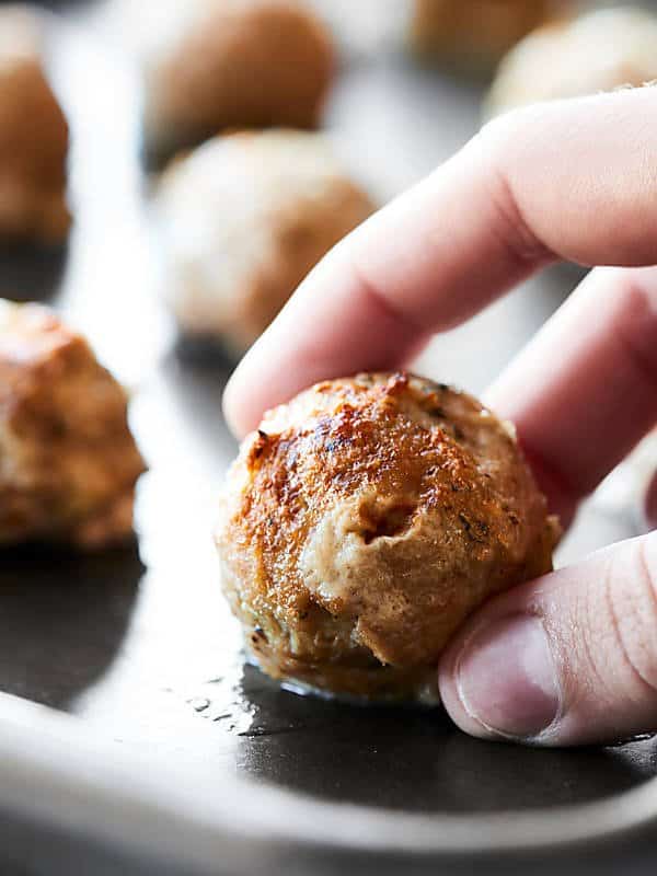 Turkey meatball being picked up off baking sheet