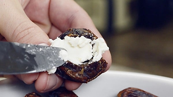 Goat cheese being spread into pitted date