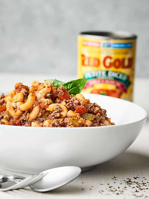 Bowl of goulash side view with can of diced tomatoes in the background