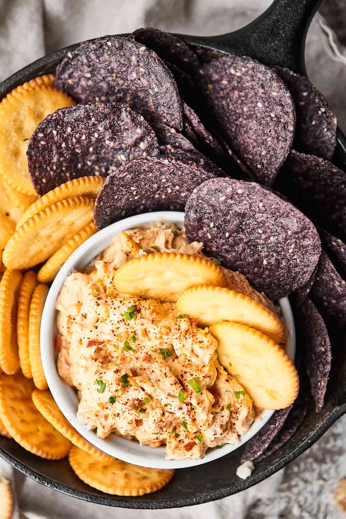 Bowl of crack dip on plate with crackers and chips above