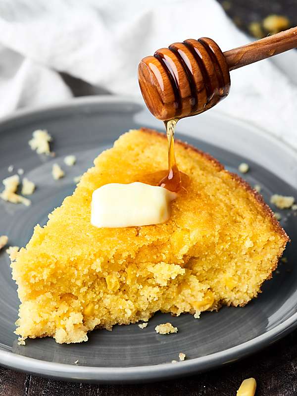 Honey being drizzled on piece of cornbread with butter