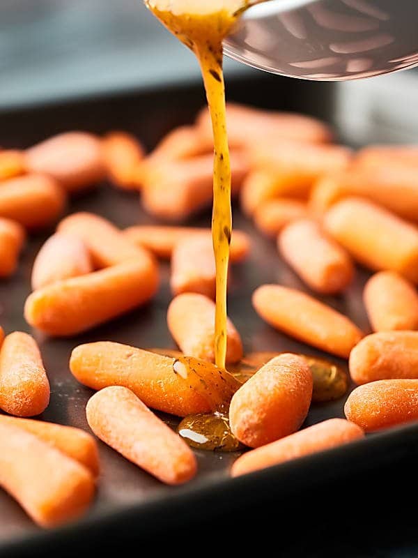 honey being drizzled over carrots on baking sheet