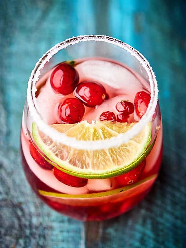cup of cranberry pomegranate margarita with lime, cranberries, and salt above