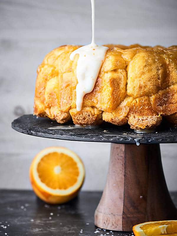 mimosa monkey bread on cake stand, icing being drizzled