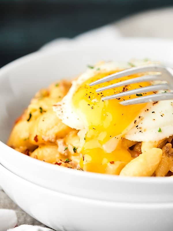 bowl of mac and cheese with egg on top cut with fork side view