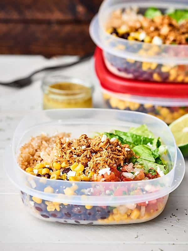 Container of chicken burrito bowl in front of two stacked burrito bowl containers