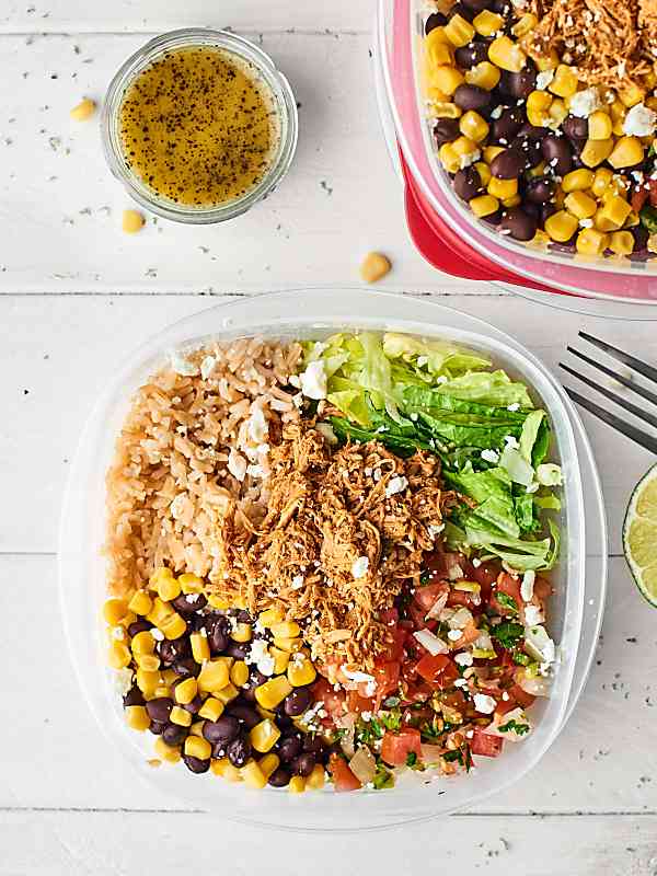 Overhead of chicken burrito bowl next to bowl of dressing