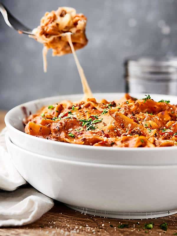one pot lasagna in bowl with fork taking bite cheese pull