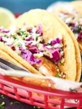 Healthy Baked Fish Tacos! Tilapia + spices + loads of lime all piled into a corn tortilla and topped with a fresh, crunchy slaw! Healthy easy deliciousness for the win! showmetheyummy.com #fishtacos #healthy #bakedfishtaco