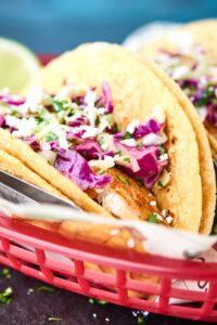 Healthy Baked Fish Tacos! Tilapia + spices + loads of lime all piled into a corn tortilla and topped with a fresh, crunchy slaw! Healthy easy deliciousness for the win! showmetheyummy.com #fishtacos #healthy #bakedfishtaco