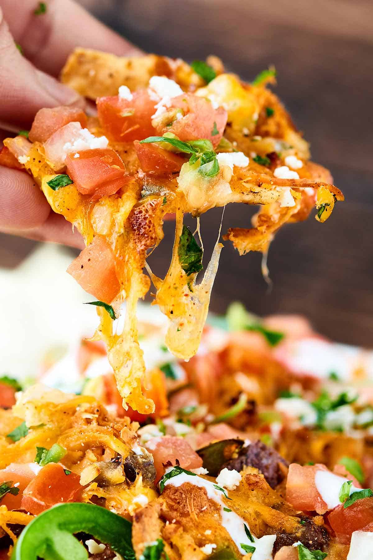 Closeup of chip being taken out of dish of loaded chicken nachos