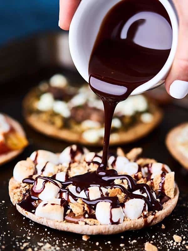 melted chocolate being poured on mini dessert smores pizza