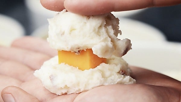 cheese cube being sandwiched between mashed potato balls