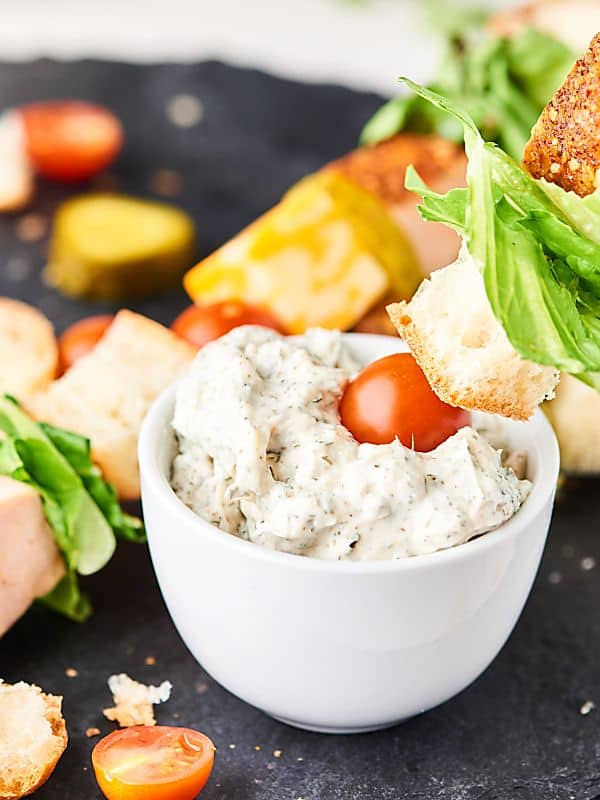 sandwich kebab being dipped into bowl of dill dipping sauce