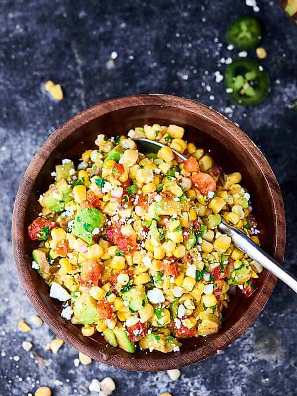 Bowl of grilled corn salsa with spoon above