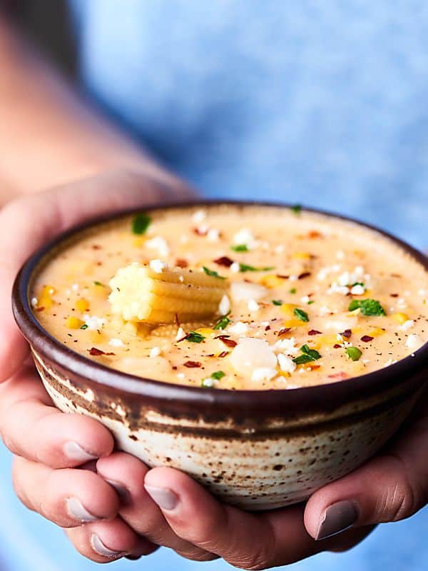 bowl of corn chowder held in two hands