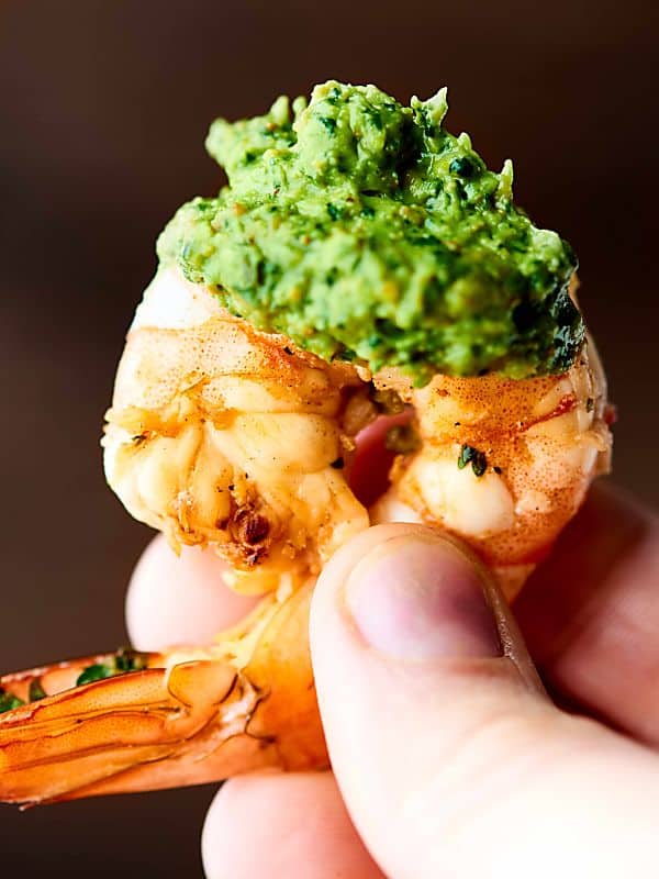 piece of grilled shrimp being held with avocado pesto sauce on it