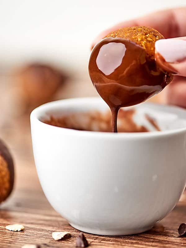 pumpkin energy bite being dipped into bowl of melted chocolate