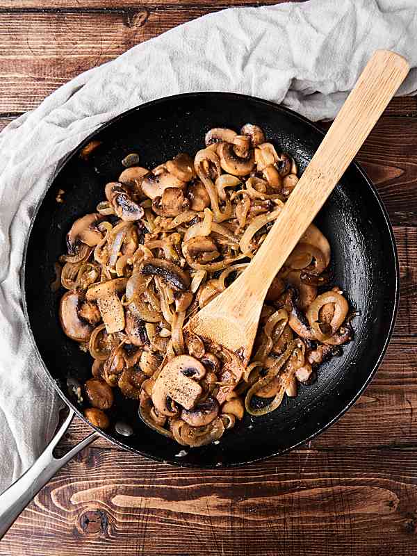 Cooked mushrooms in a skillet with wooden spoon above